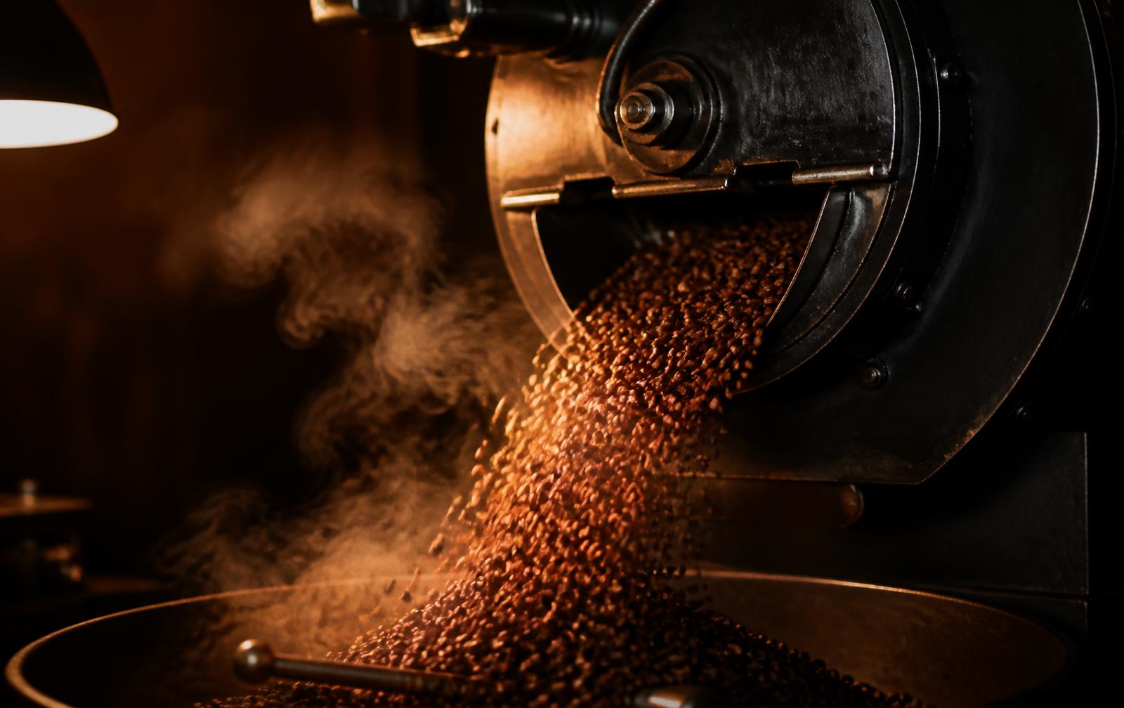 Freshly roasted coffee beans tumbling from a drum roaster into the cooling tray, lit by warm amber light.